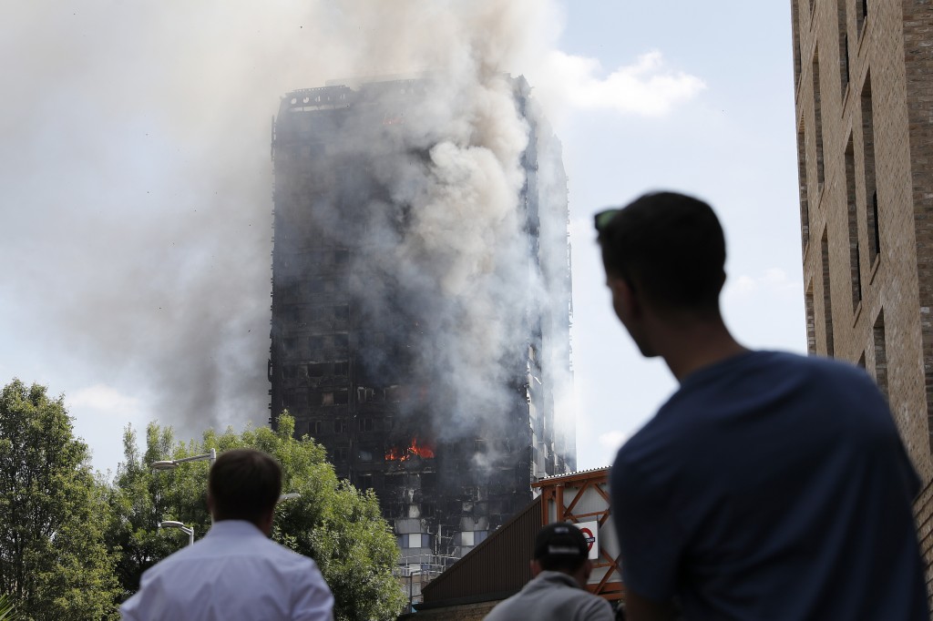 Pedestrians look up towards Grenfell Tower, a residential block of flats in west London on June 14, 2017, as firefighters continue to control a fire that engulfed the building in the early hours of the morning. Shaken survivors of a blaze that ravaged a west London tower block told Wednesday of seeing people trapped or jump to their doom as flames raced towards the building's upper floors and smoke filled the corridors. / AFP PHOTO / Adrian DENNIS