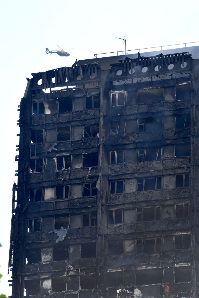 A helicopter hovers near the burnt-out facade of Grenfell Tower after a fire ripped through the building in west London on June 14, 2017. At least six people were killed Wednesday when a massive fire tore through a London apartment block overnight, with survivors voicing anger over longstanding safety fears at the 24-storey Grenfell Tower. / AFP PHOTO / Ben STANSALL