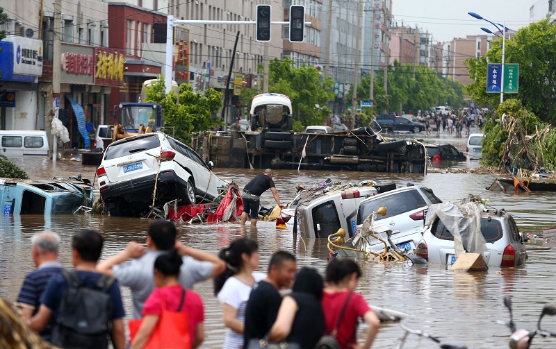 This photo taken on July 14, 2017 shows people looking at submerged cars in a flooded street in Yongji, a county under the administration of the city of Jilin in northeast China's Jilin province. Heavy rains caused flooding that left 18 people dead and another 18 missing around Jilin, with more than 110,000 evacuated when flooding hit the city on July 13 and 14. / AFP PHOTO / STR / China OUT