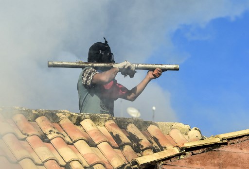 An opposition demonstrator on a roof aims a makeshift firecracker launcher at riot police during clashes ensuing an anti-government protest in Caracas, on July 26, 2017. Venezuelans blocked off deserted streets Wednesday as a 48-hour opposition-led general strike aimed at thwarting embattled President Nicolas Maduro's controversial plans to rewrite the country's constitution got underway. / AFP PHOTO / RONALDO SCHEMIDT