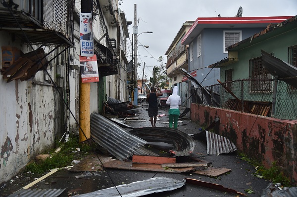 Men walk past damaged homes after the passage of Hurricane Maria, in San Juan, Puerto Rico, on September 20, 2017. Maria slammed into Puerto Rico on, cutting power on most of the US territory as terrified residents hunkered down in the face of the island's worst storm in living memory. After leaving a deadly trail of destruction on a string of smaller Caribbean islands, Maria made landfall on Puerto Rico's southeast coast around daybreak, packing winds of around 150mph (240kph).  / AFP PHOTO / Hector RETAMAL