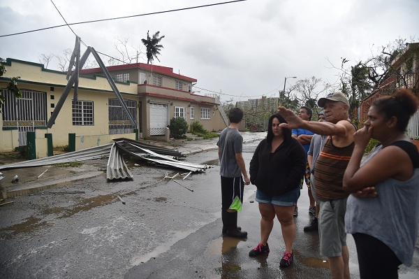 Inhabitants of Puerto Nuevo neighbourhood stand next to roof blown off during the passage of Hurricane Maria, in San Juan, Puerto Rico, on September 20, 2017. Maria slammed into Puerto Rico on, cutting power on most of the US territory as terrified residents hunkered down in the face of the island's worst storm in living memory. After leaving a deadly trail of destruction on a string of smaller Caribbean islands, Maria made landfall on Puerto Rico's southeast coast around daybreak, packing winds of around 150mph (240kph).  / AFP PHOTO / HECTOR RETAMAL