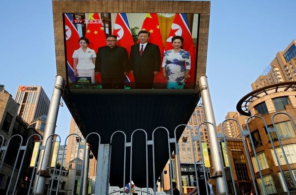  La gente pasa en bicicleta frente a una pantalla de televisión gigante que transmite la reunión del líder norcoreano, Kim Jong-un, y el presidente chino, Xi Jinping, este martes 19 de junio en Pekín 
