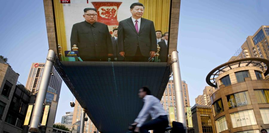Gente pasa frente a una pantalla gigante que transmite la reunión del líder norcoreano Kim Jong Un con el presidente chino Xi Jinping